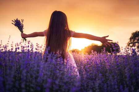Happy little girl with dress enjoying lavender field with bouquet of flowersの写真素材