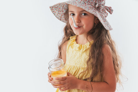 Beautiful little girl with spoon in mouth eating tasty cream. Eating yummy ice cream is funの写真素材
