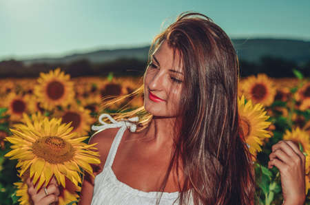 Beautiful girl in a field, holding small sunflowerの写真素材