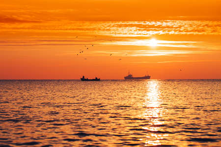 Fisherman sailling with his boat on beautiful sunrise over the seaの写真素材