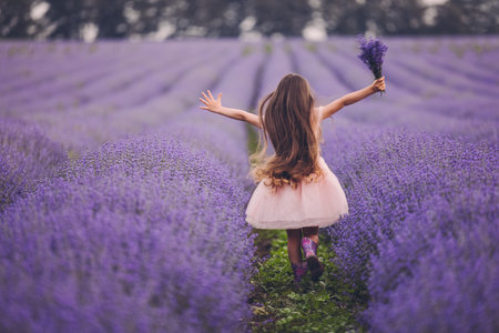 Happy little girl with dress enjoying lavender field with bouquet of flowersの写真素材