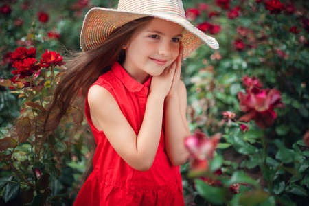 Beautiful little girl in roses garden in park. Charming woman smiling outdoor with flowers.の写真素材