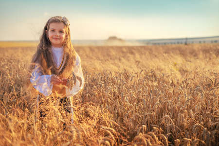 Young girl with traditional Bulgarian folklore costume at the agricultural wheat field during harvest time with industrial combine machineの写真素材