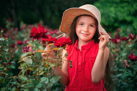 Beautiful little girl in roses garden in park. Charming woman smiling outdoor with flowers.の写真素材