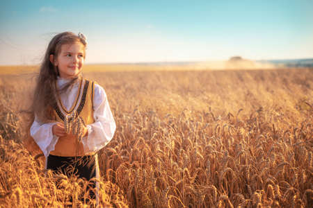 Young girl with traditional Bulgarian folklore costume at the agricultural wheat field during harvest time with industrial combine machineの写真素材