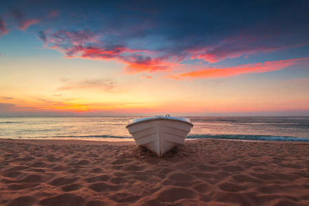 Tropical Seascape with a boat on sandy beach at cloudy sunrise or sunsetの写真素材