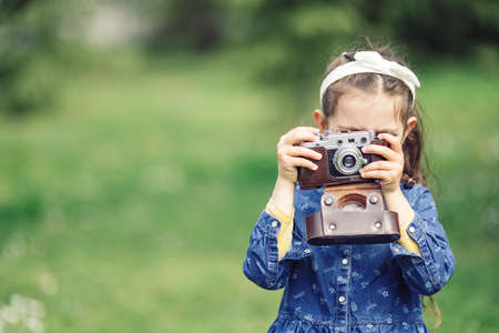 Little girl with old vintage camera making photos of surrounding nature in the parkの写真素材