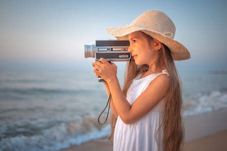 Girl with a retro vintage camera taking photos and film of a beautiful sea sunrise and beachの写真素材