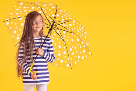 Happy emotional girl laughing with umbrella on colored yellow background. Autumn, spring season.の写真素材