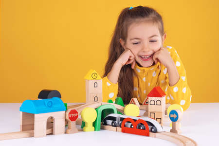 Cute kid, little girl playing with wooden toys train and railway roadの写真素材