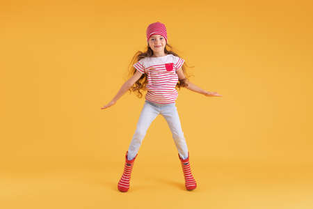 Happy emotional girl jumping on colored yellow background. Autumn, spring season.の写真素材