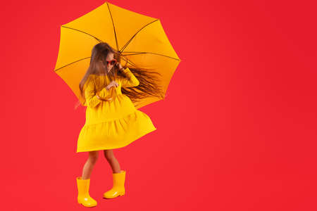 Happy emotional girl laughing with umbrella on colored red background. Autumn, spring season.の写真素材