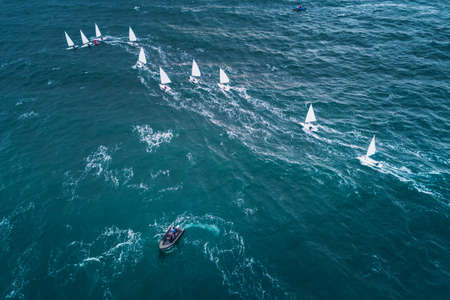 Regatta sailing ship yachts with white sails at opened sea. Aerial view of sailboat in windy condition.の写真素材