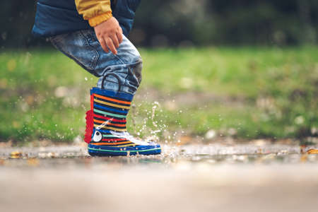 Happy little kid boy jumping on rainy puddle in autumn on natureの写真素材