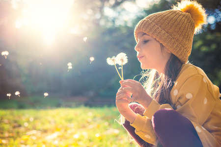 Little beautiful girl blowing dandelion on the meadow at sunsetの写真素材