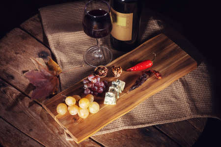 Red wine bottle, grape, cheese, wineglass and chili pepper on wooden boardの写真素材