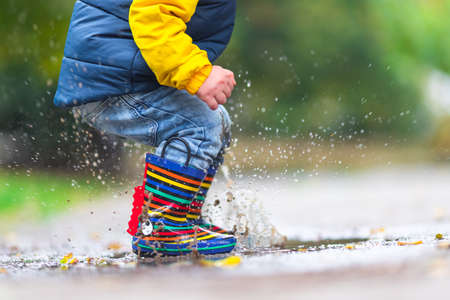 Happy little kid boy jumping on rainy puddle in autumn on natureの写真素材