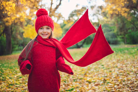 Autumn park and happy little girl playing with red scarfの写真素材