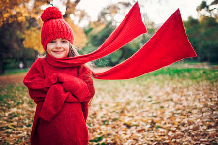 Autumn park and happy little girl playing with red scarfの写真素材