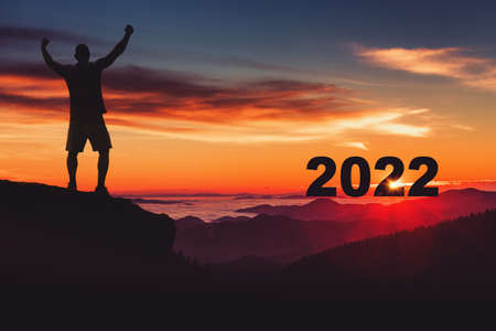 Man silhouette on the mountain top watching the sunrise and 2022 years while celebrating.の写真素材