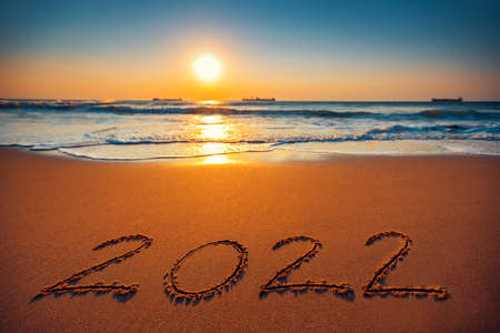 Happy New Year 2022 concept, lettering on the beach. Sea sunrise.