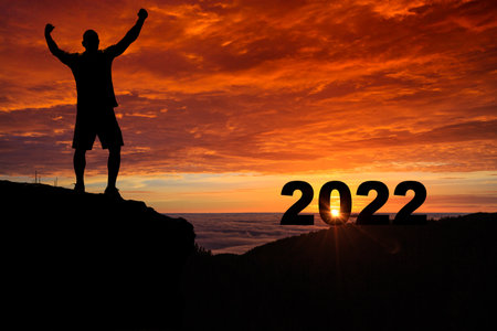 Man silhouette on the mountain top watching the sunrise and 2022 years while celebrating.の写真素材
