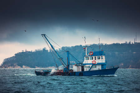 Fishing boat and fisherman in the sea, foggy morning over the water.の写真素材