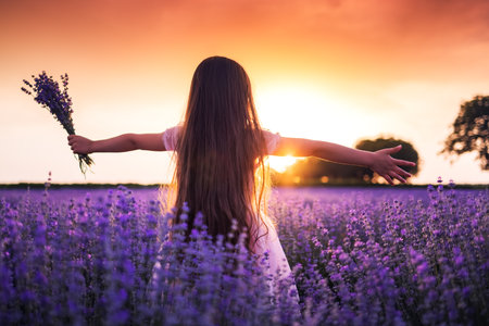 Happy little girl with dress enjoying lavender field with bouquet of flowersの写真素材