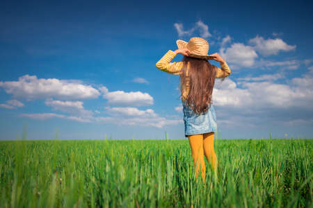 Green wheat field landscape and happy farmer girl playing with straw hatの写真素材