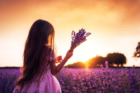 Happy little girl with dress enjoying lavender field with bouquet of flowersの写真素材