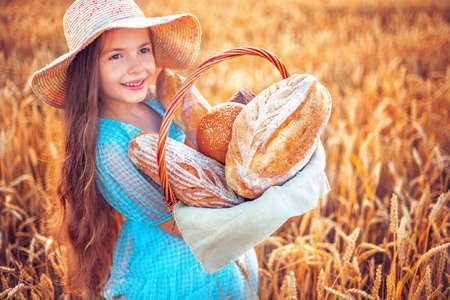 Beautiful girl woman in traditional Bulgarian folklore dress holding wicker basket with homemade breads in wheat fieldの写真素材