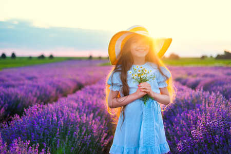 Happy little girl with dress enjoying lavender field with bouquet of flowersの写真素材