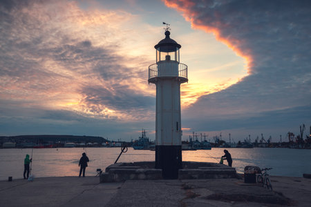 Coastal lighthouse scenic sunset with dramatic clouds in the harbour. Beacon near the beach in...