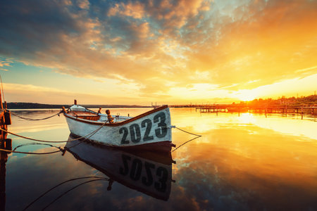 2023 concept Fishing Boat on Varna lake with a reflection in the water at sunset.の写真素材
