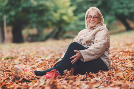 Happy beautiful senior woman enjoying nature in park in autumnの写真素材