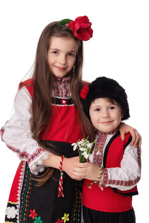 Bulgarian kids boy and girl in traditional folklore costumes with spring flowers snowdrop and handcraft wool bracelet martenitsa symbol of Baba Martaの写真素材