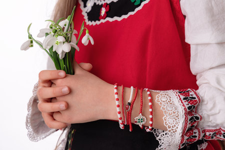 Bulgarian girl in traditional folklore costumes with spring flowers snowdrop and handcraft wool bracelet martenitsa symbol of Baba Martaの写真素材