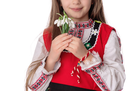 Bulgarian girl in traditional folklore costumes with spring flowers snowdrop and handcraft wool bracelet martenitsa symbol of Baba Martaの写真素材