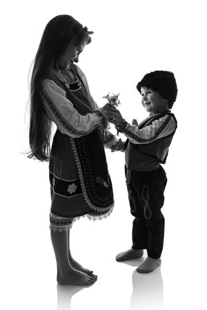 Bulgarian kids boy and girl in traditional folklore costumes with spring flowers snowdrop and handcraft wool bracelet martenitsa symbol of Baba Martaの写真素材