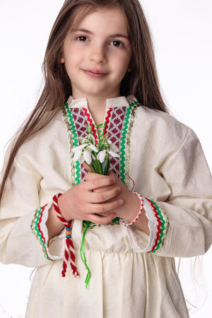 Bulgarian girl in traditional folklore costumes with spring flowers snowdrop and handcraft wool bracelet martenitsa symbol of Baba Martaの写真素材