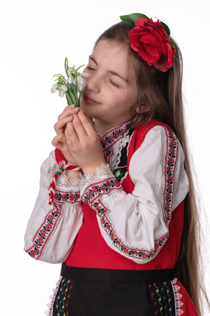 Bulgarian girl in traditional folklore costumes with spring flowers snowdrop and handcraft wool bracelet martenitsa symbol of Baba Martaの写真素材