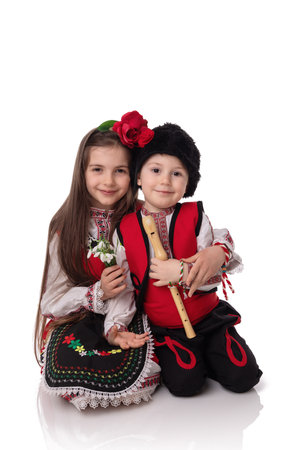 Bulgarian kids boy and girl in traditional folklore costumes with spring flowers snowdrop and handcraft wool bracelet martenitsa symbol of Baba Martaの写真素材