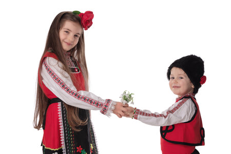 Bulgarian kids boy and girl in traditional folklore costumes with spring flowers snowdrop and handcraft wool bracelet martenitsa symbol of Baba Martaの写真素材