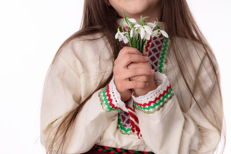 Bulgarian girl in traditional folklore costumes with spring flowers snowdrop and handcraft wool bracelet martenitsa symbol of Baba Martaの写真素材