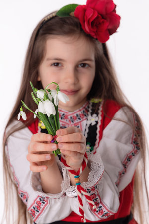 Bulgarian girl in traditional folklore costumes with spring flowers snowdrop and handcraft wool bracelet martenitsa symbol of Baba Martaの写真素材