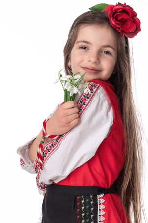 Bulgarian girl in traditional folklore costumes with spring flowers snowdrop and handcraft wool bracelet martenitsa symbol of Baba Martaの写真素材