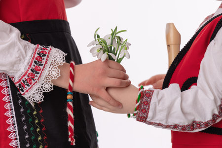Bulgarian kids boy and girl in traditional folklore costumes with spring flowers snowdrop and handcraft wool bracelet martenitsa symbol of Baba Martaの写真素材