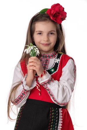 Bulgarian girl in traditional folklore costumes with spring flowers snowdrop and handcraft wool bracelet martenitsa symbol of Baba Martaの写真素材