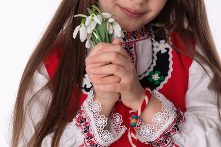 Bulgarian girl in traditional folklore costumes with spring flowers snowdrop and handcraft wool bracelet martenitsa symbol of Baba Martaの写真素材