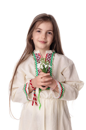 Bulgarian girl in traditional folklore costumes with spring flowers snowdrop and handcraft wool bracelet martenitsa symbol of Baba Martaの写真素材